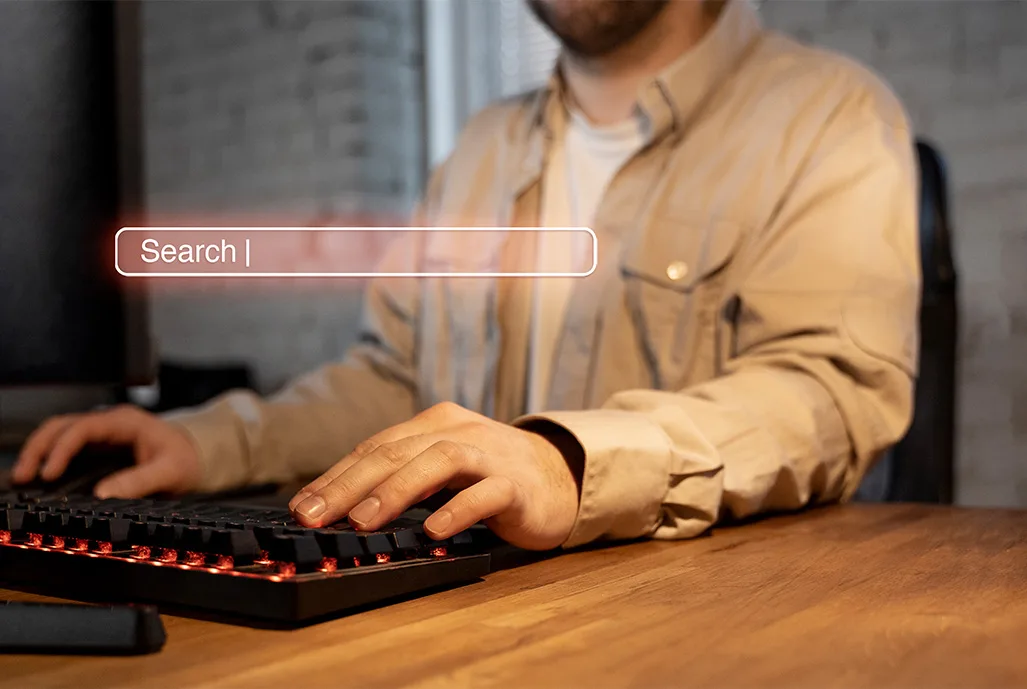 Pessoa digitando no teclado do computador com uma barra de busca em destaque na frente da tela