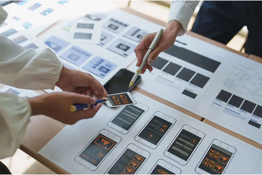 Equipe planejando o layout de um site e de um aplicativo com wireframes impressos sobre a mesa